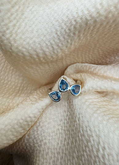 Bague en argent avec trois pierres taille poire bleues, sur du tissu