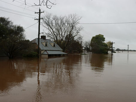 House submerged to its roofline in brown floodwater, with power poles standing in the water