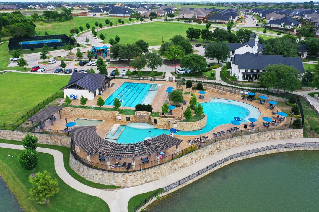 Aerial view of The Club at Mustang Lakes pools, lake edge, recreation grounds, and surrounding homes.