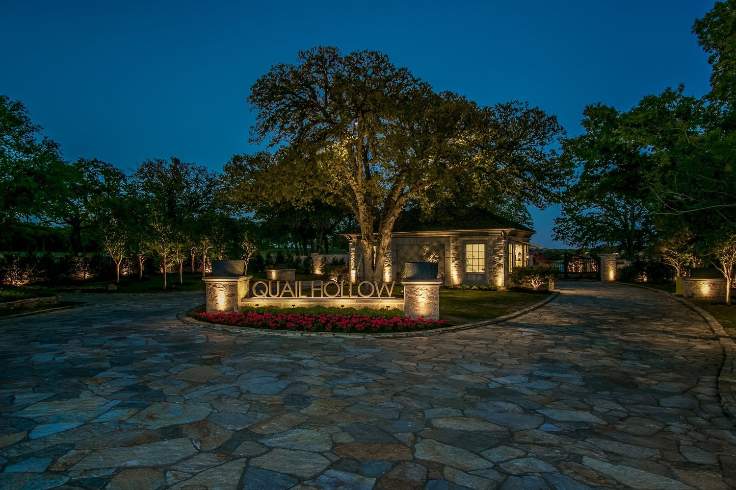 Illuminated Quail Hollow entrance, gatehouse and stone drive at dusk.