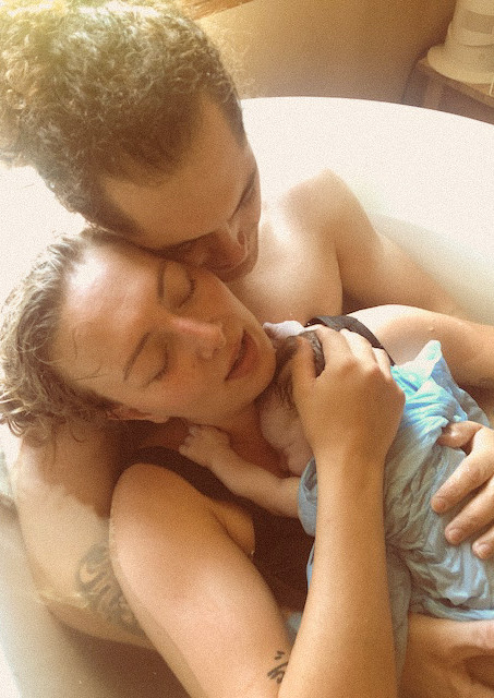 Husband and wife sitting holding newborn baby in bathtub after delivering baby at a homebirth.
