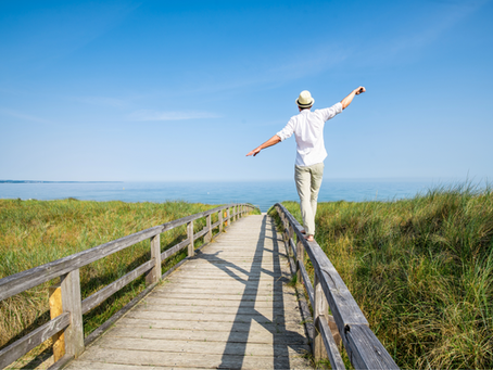 Man balancing on a fence beam near the ocean on a beautiful day