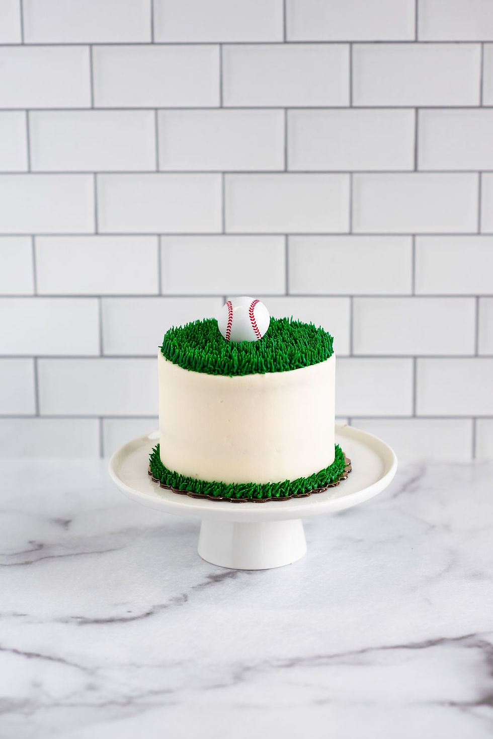 white buttercream smash cake with piped green grass texture on a white cake stand.