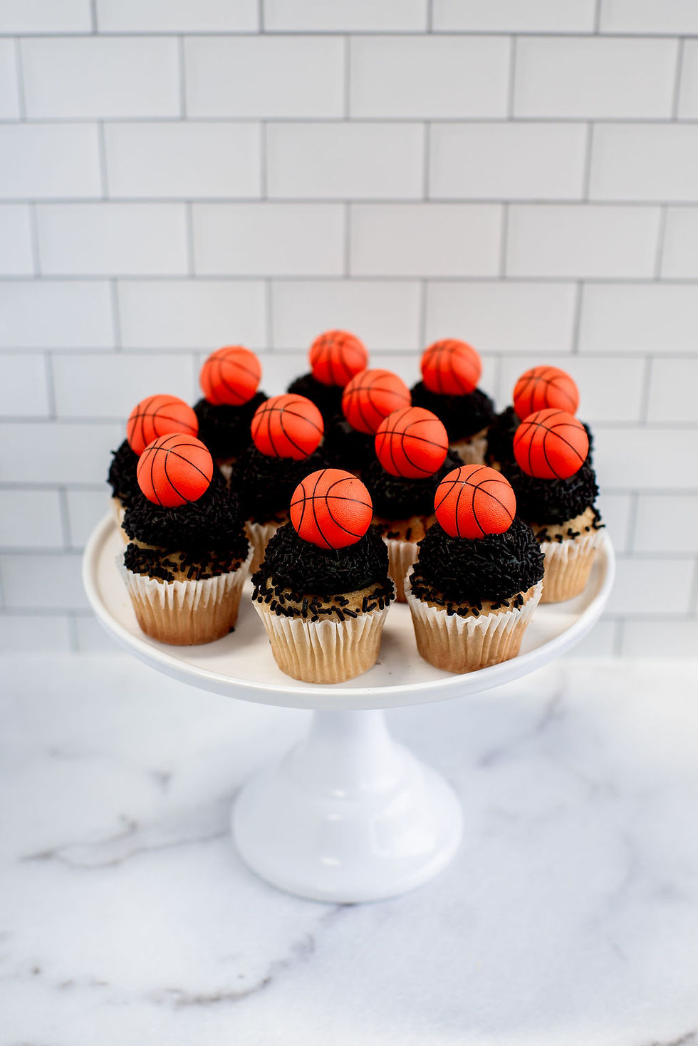 A display of basketball-themed cupcakes topped with buttercream frosting, chocolate sprinkles, and plastic basketball toppers