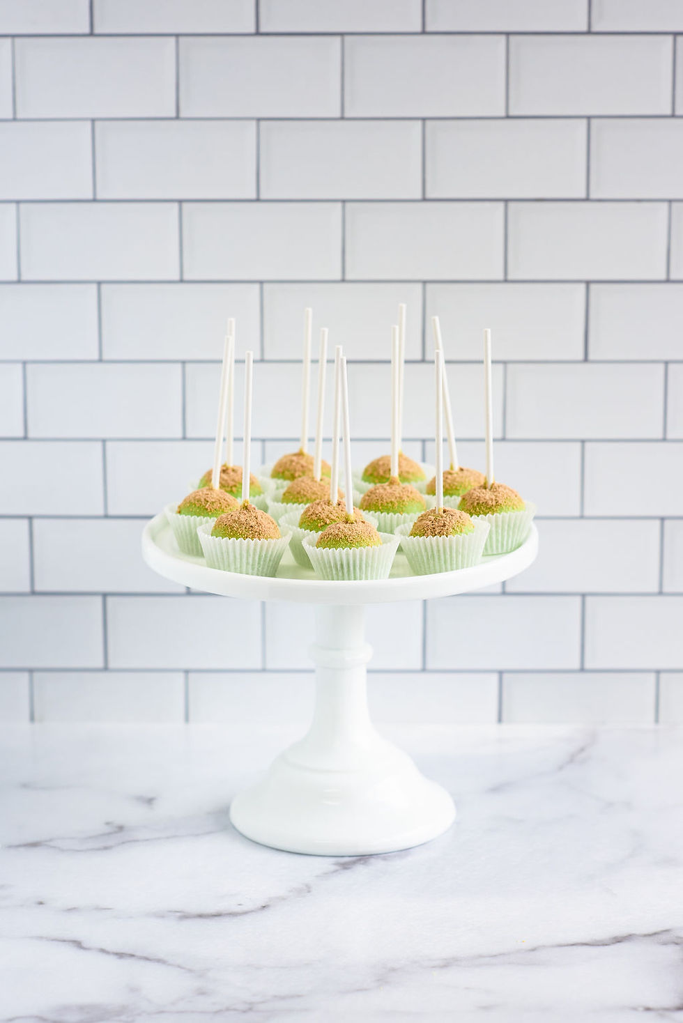 Thumbnail: A display of key lime cake pops coated in light green chocolate and topped with graham cracker crumbs,