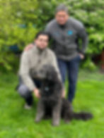 Tim und Horst posieren zusammen mit ihrem Hund Arm in Arm auf einer Wiese