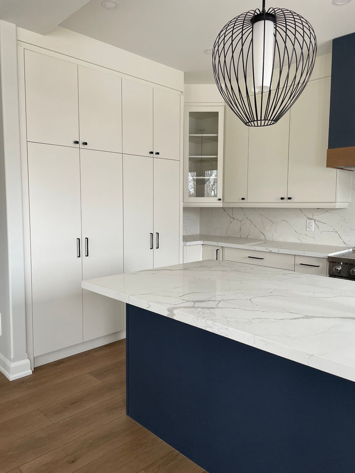 White kitchen cabinetry with navy island and decorative vent hood. Design by Caroline Loon Designs