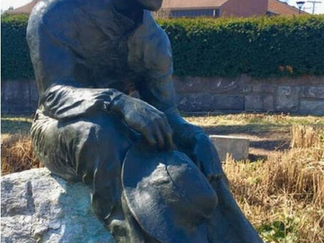 bronze young male appears seated, hat in hand, under the shade of an oak tree, engaged in thought