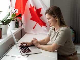 A woman working on a laptop in an office space with a Canadian flag.