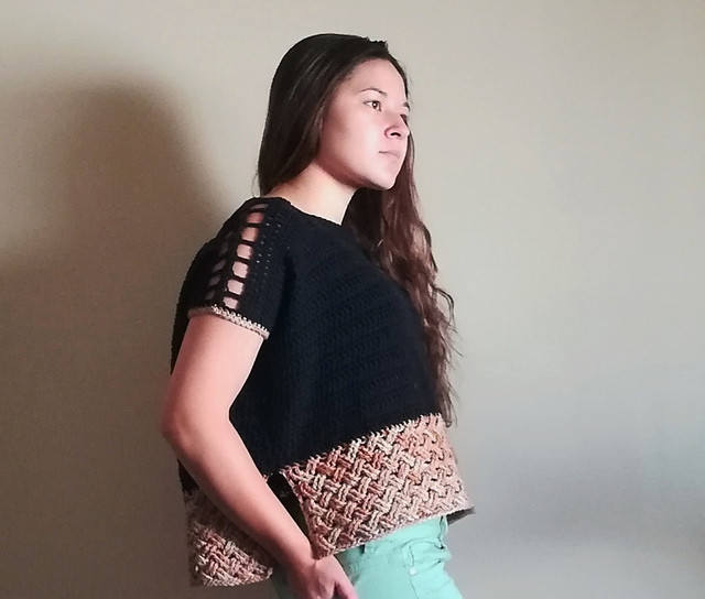 a woman wearing a crocheted drop-sleeve top with large eyelets on the shoulders and a woven pattern along the bottom.