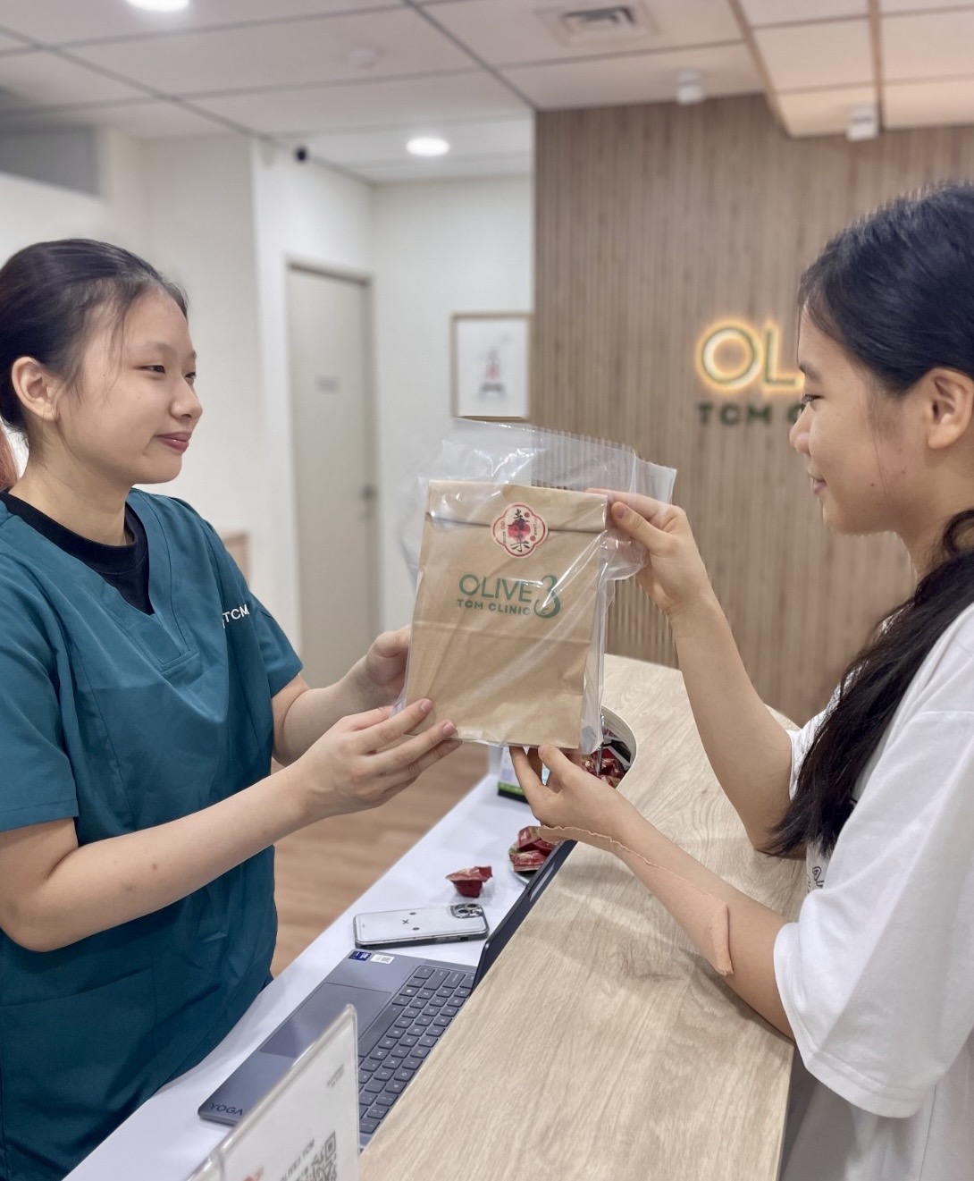 Olive3 TCM Clinic staff handing a clinic bag to a visitor at reception