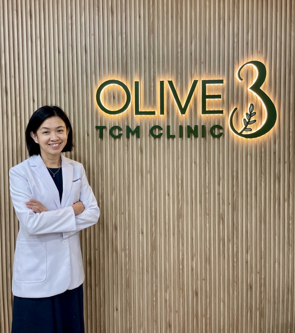 Physician Koh Soo Hoon beside the Olive3 TCM Clinic sign in Singapore