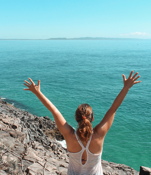 Woman reaching her arms out wide while standing on a cliff admiring the ocean