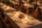Elegant dining setup with candlelit tables, white tablecloths, and floral centerpieces in a warm, softly lit restaurant setting.