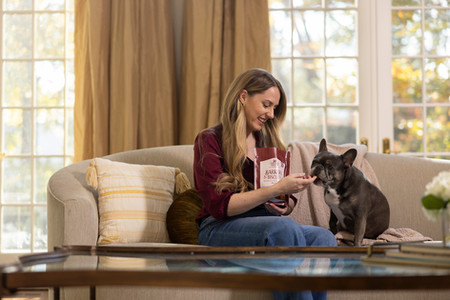 Woman sitting on sofa feeding dog a traet
