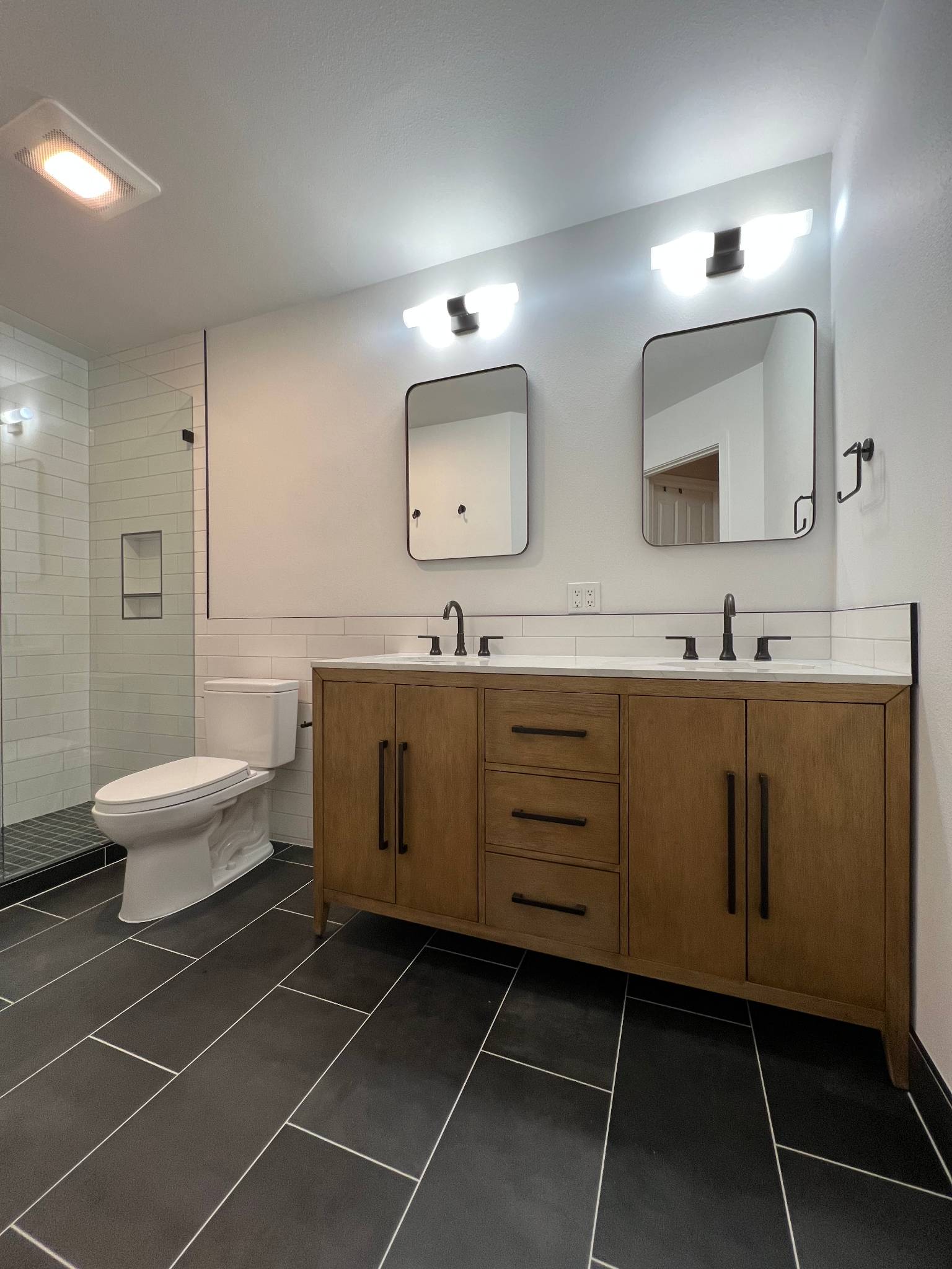 After — wide double vanity with dual lit mirrors, full room view of completed remodel