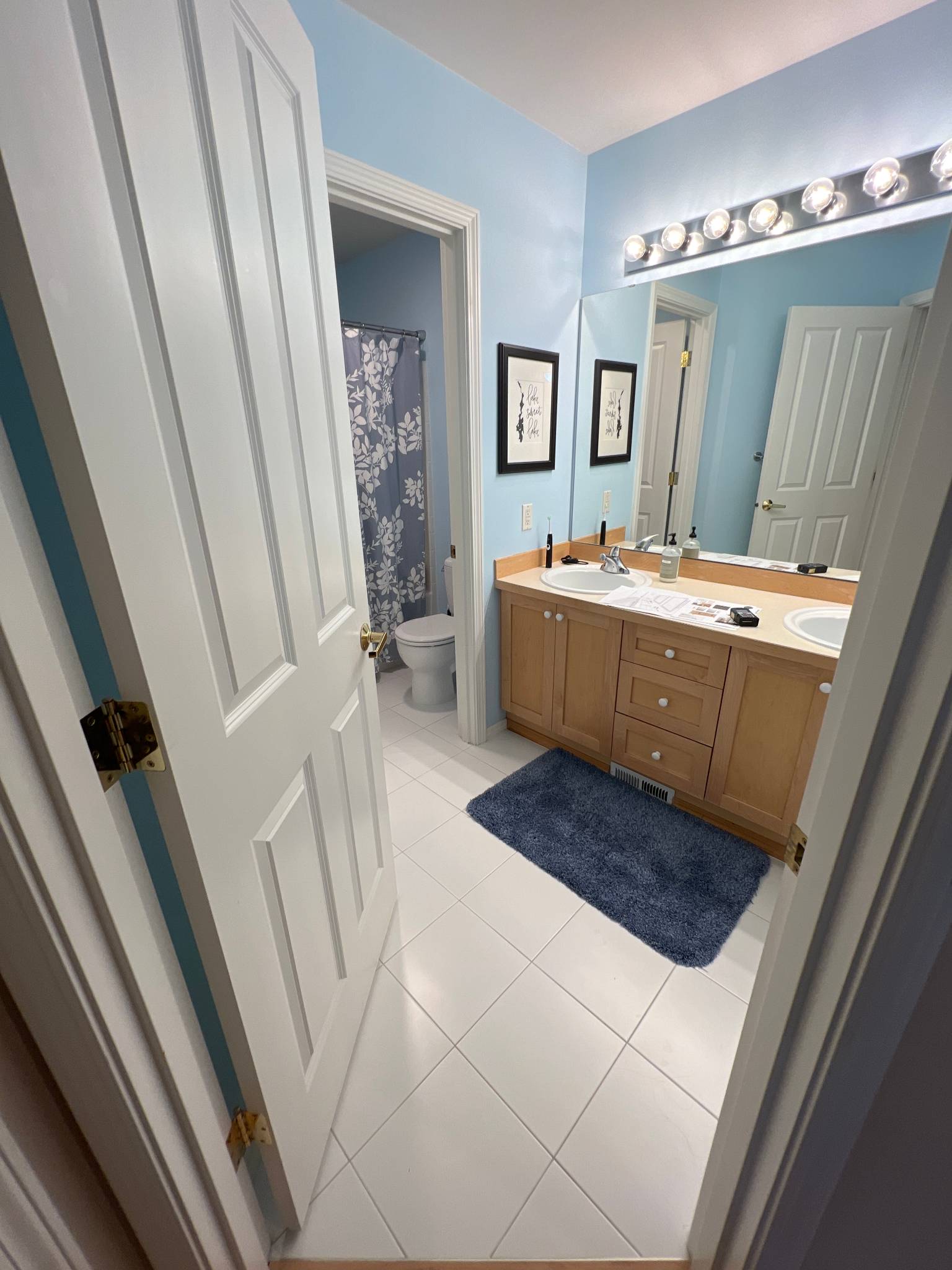 Before — builder-grade bathroom from doorway, blue paint, oak vanity and old fixtures