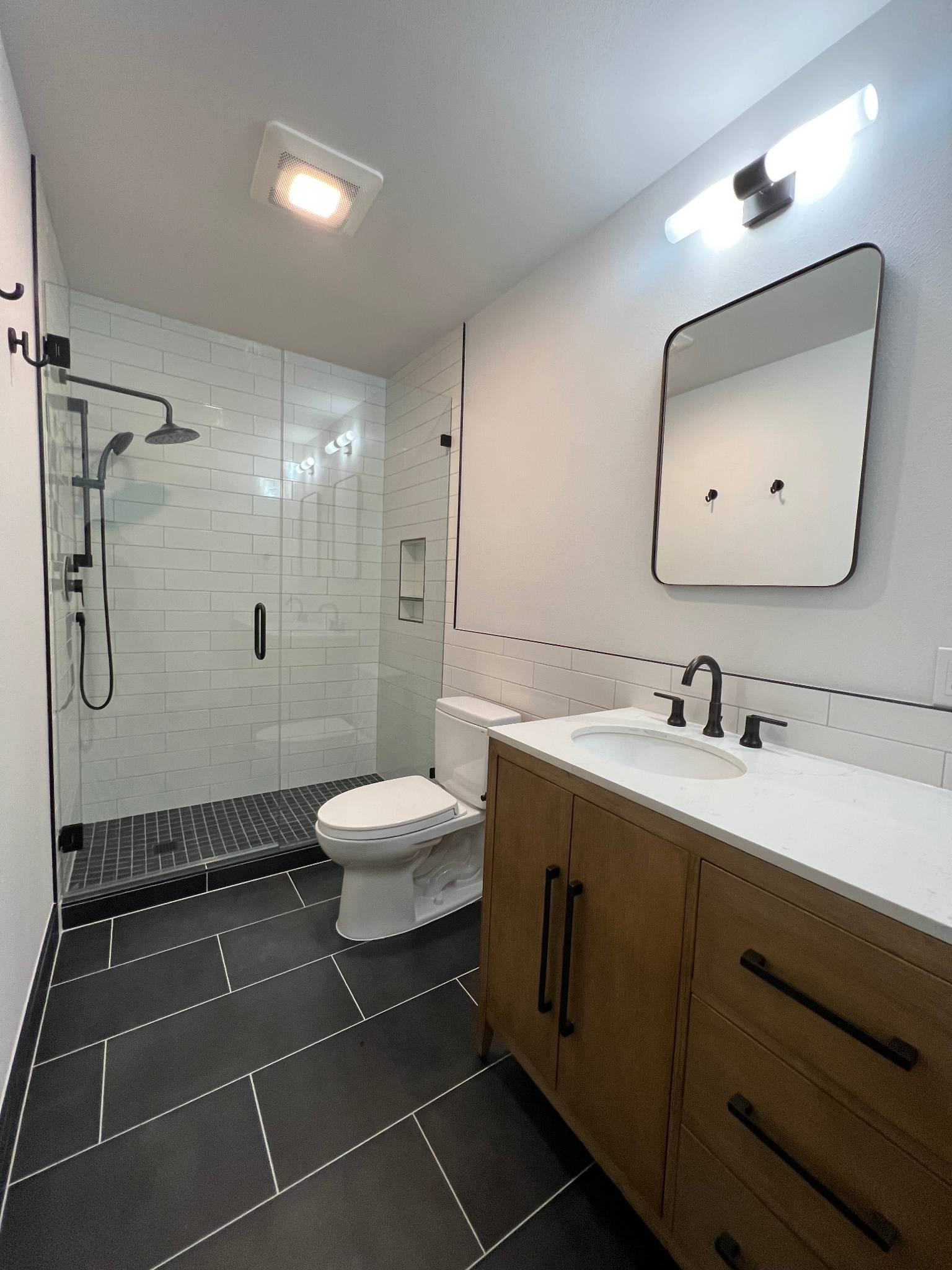 After — side angle of shower and vanity showing rain head and mosaic floor