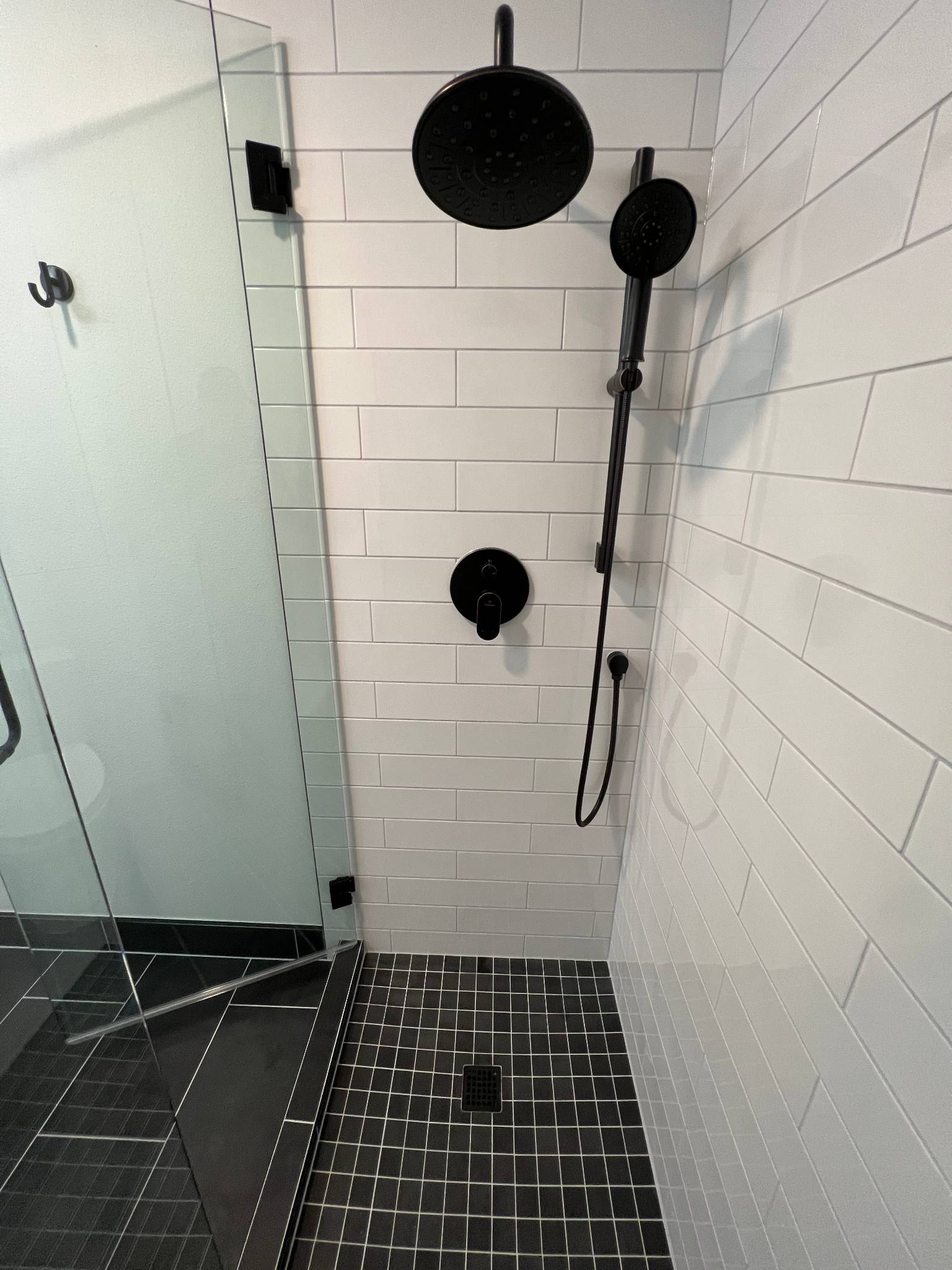 After — shower interior with matte black rain head, hand shower, white subway tile and mosaic floor