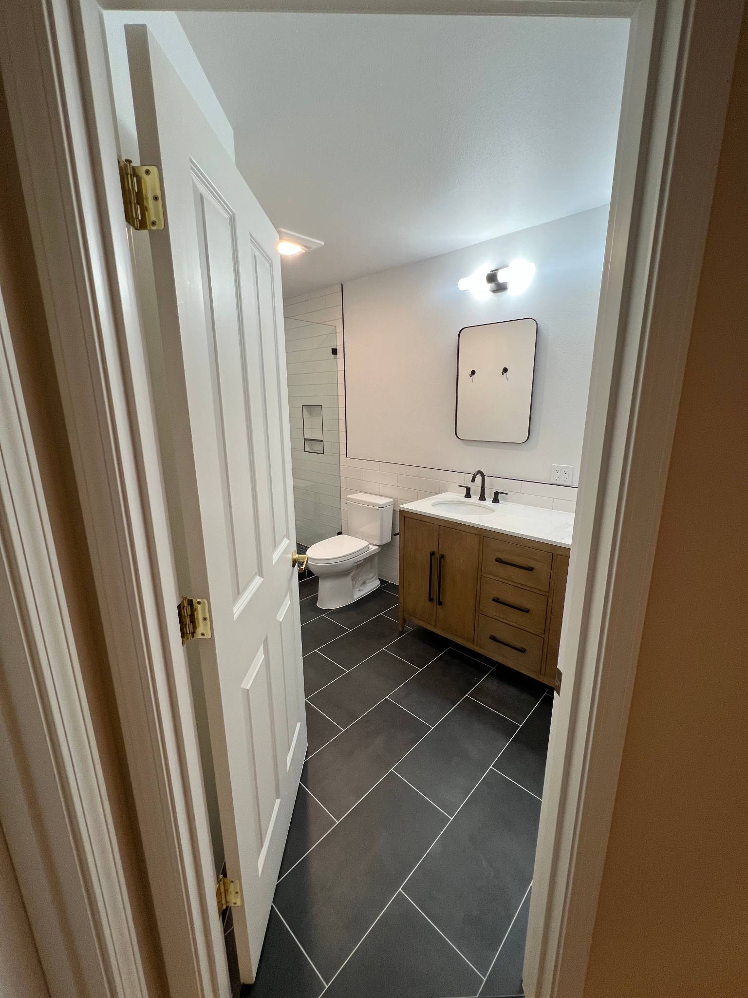 After — frameless shower and vanity from doorway showing the complete remodeled space