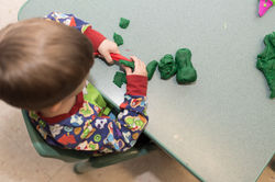 Overhead shot of child cutting green play-dough into small pieces
