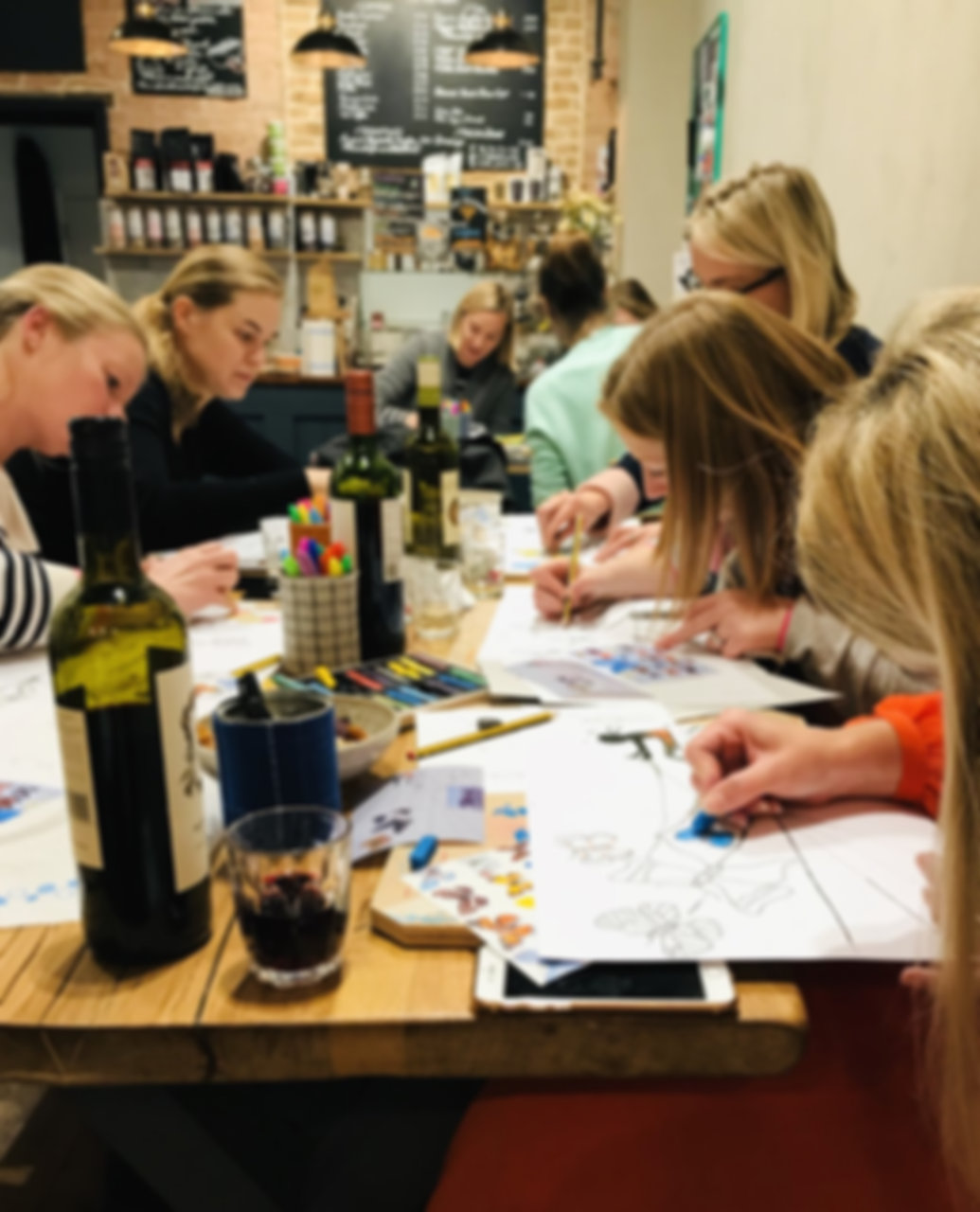 Women sitting at a table with glasses of wine, sketching and colouring