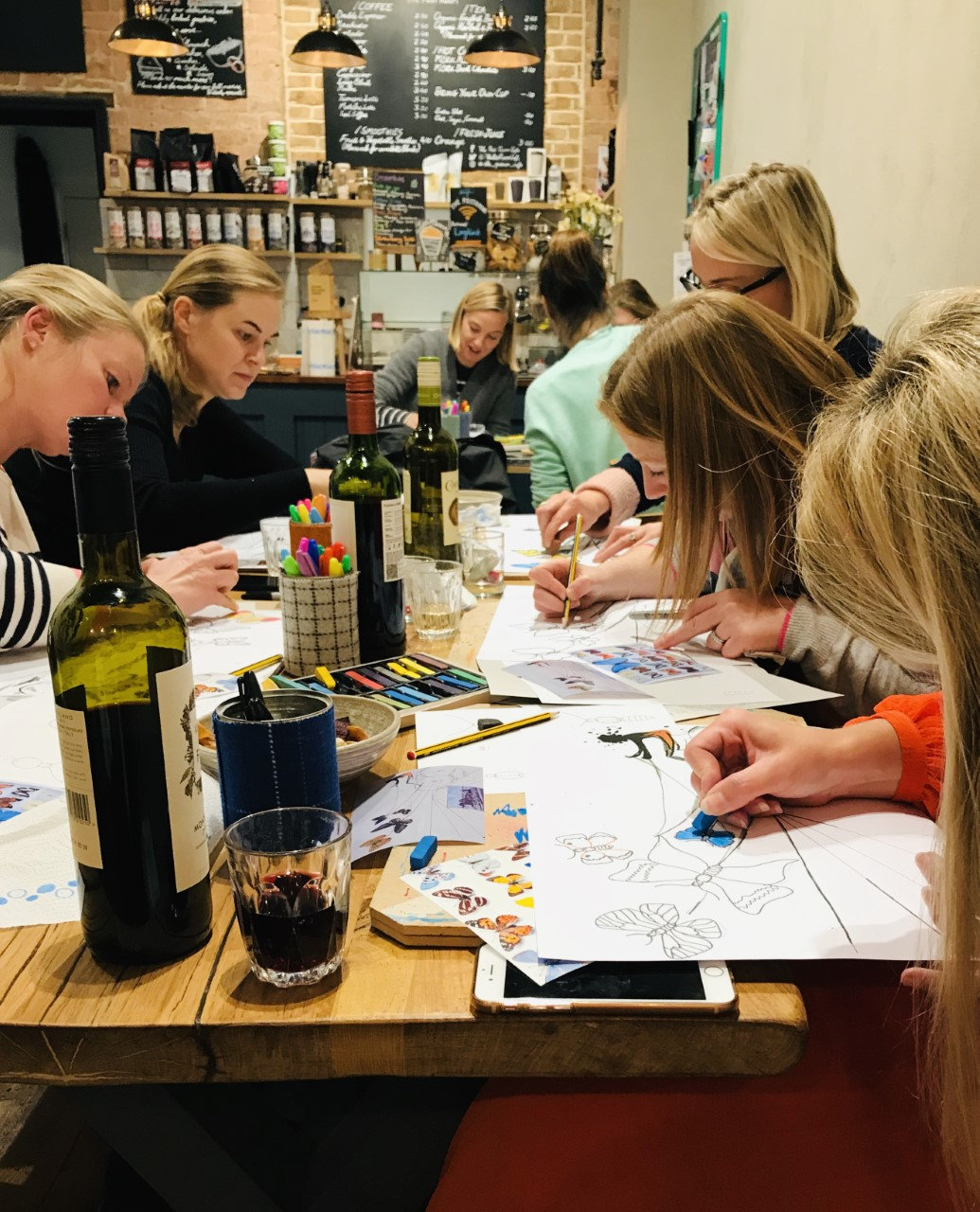 Women sitting at a table with glasses of wine, sketching and colouring