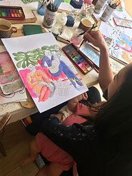 Woman holding a baby on her lap as she works on her watercolour painting
