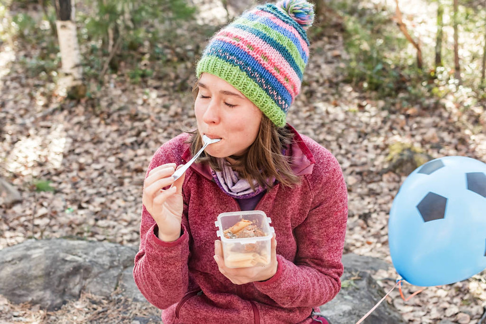 girl in a hat in the autumn forest eats from a plastic container.