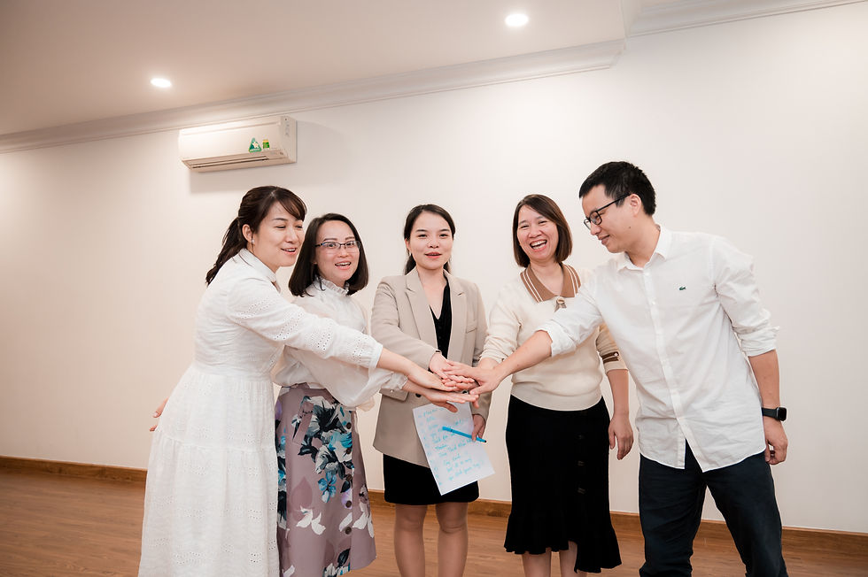 Nhóm 5 người đứng trong phòng, tay chồng lên nhau thể hiện sự đoàn kết và teamwork, cười vui vẻ.