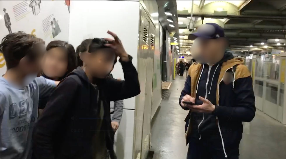 Group of people in a busy subway station, one holding a phone. Background shows industrial ceiling and walls with text and drawings.