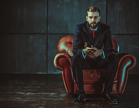 Young handsome businessman with beard in black suit sitting on chair and talking with speaker. Film