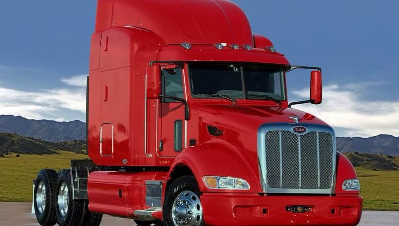 Red Peterbilt semi truck tractor parked on open road with chrome grille and sleeper cab