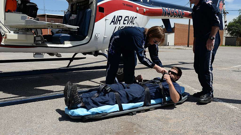 Paramedics assist a man on a stretcher by a helicopter labeled "Air Evac." The day is clear with blue skies, and they are on a paved surface.