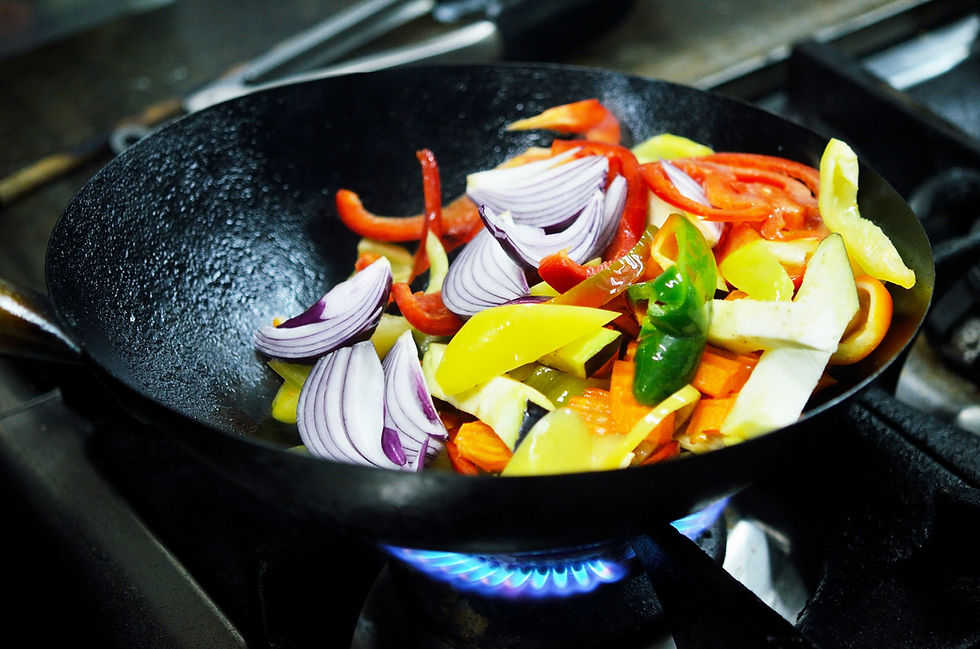 Colorful vegetables, including red onions and peppers, sizzle in a black wok on a blue flame stove, creating a vibrant cooking scene.