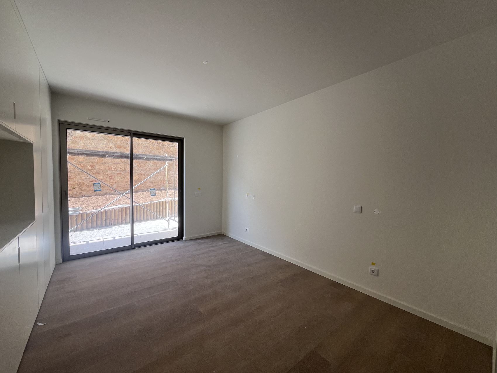Sala vazia do apartamento, pavimento de madeira e vão à esquerda, antes do projeto