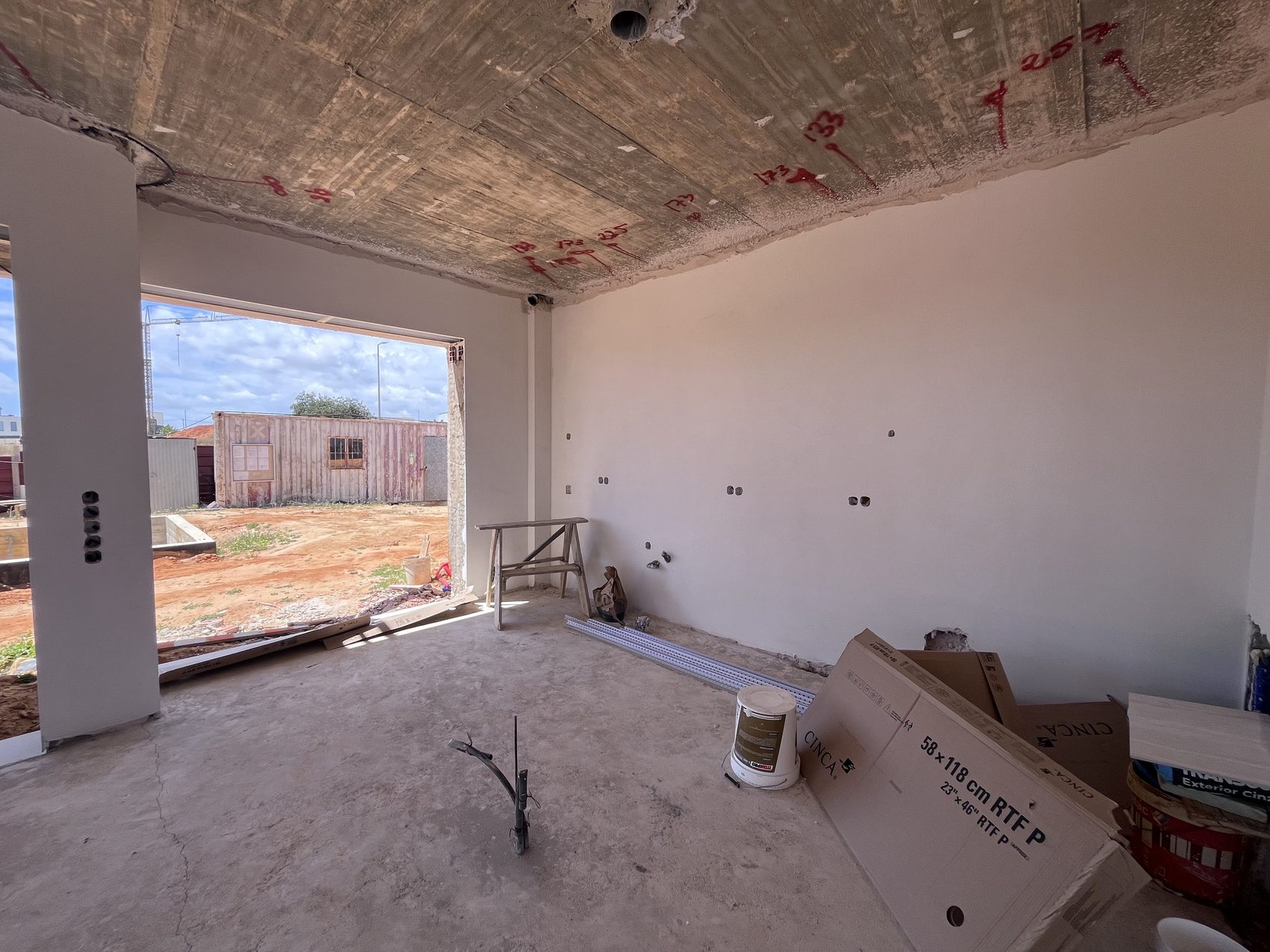 Interior da moradia em tosco, laje à vista com marcações e vão à esquerda