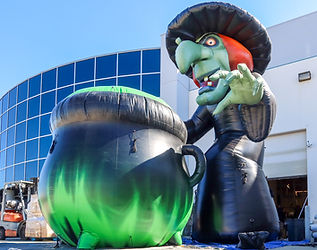 Large inflatable witch with a bubbling cauldron placed outside a commercial building for a Halloween-themed installation
