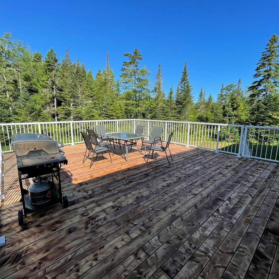 Enjoy ample outdoor living space on this expansive wood deck constructed by Thirty Four Renovations. Perfect for entertaining or simply relaxing, it features durable decking and clean white railings, set against a beautiful natural backdrop.

 Large wooden deck build with white railing by Thirty Four Renovations.