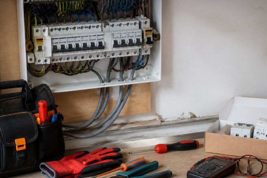 An electrician inspecting a damaged domestic electrical panel in a home utility cupboard