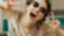 Woman with sunglasses laughing and making peace signs towards the camera.