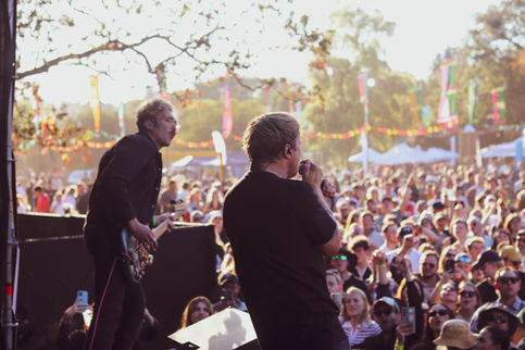 Band performing at outdoor festival with large crowd.