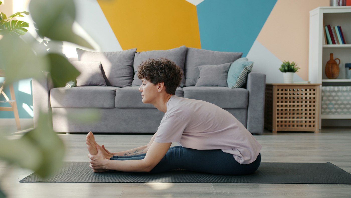 Real editorial photograph of woman stretching on yoga mat at home. Cover for Body Scanning Without Trying to Fix Yourself