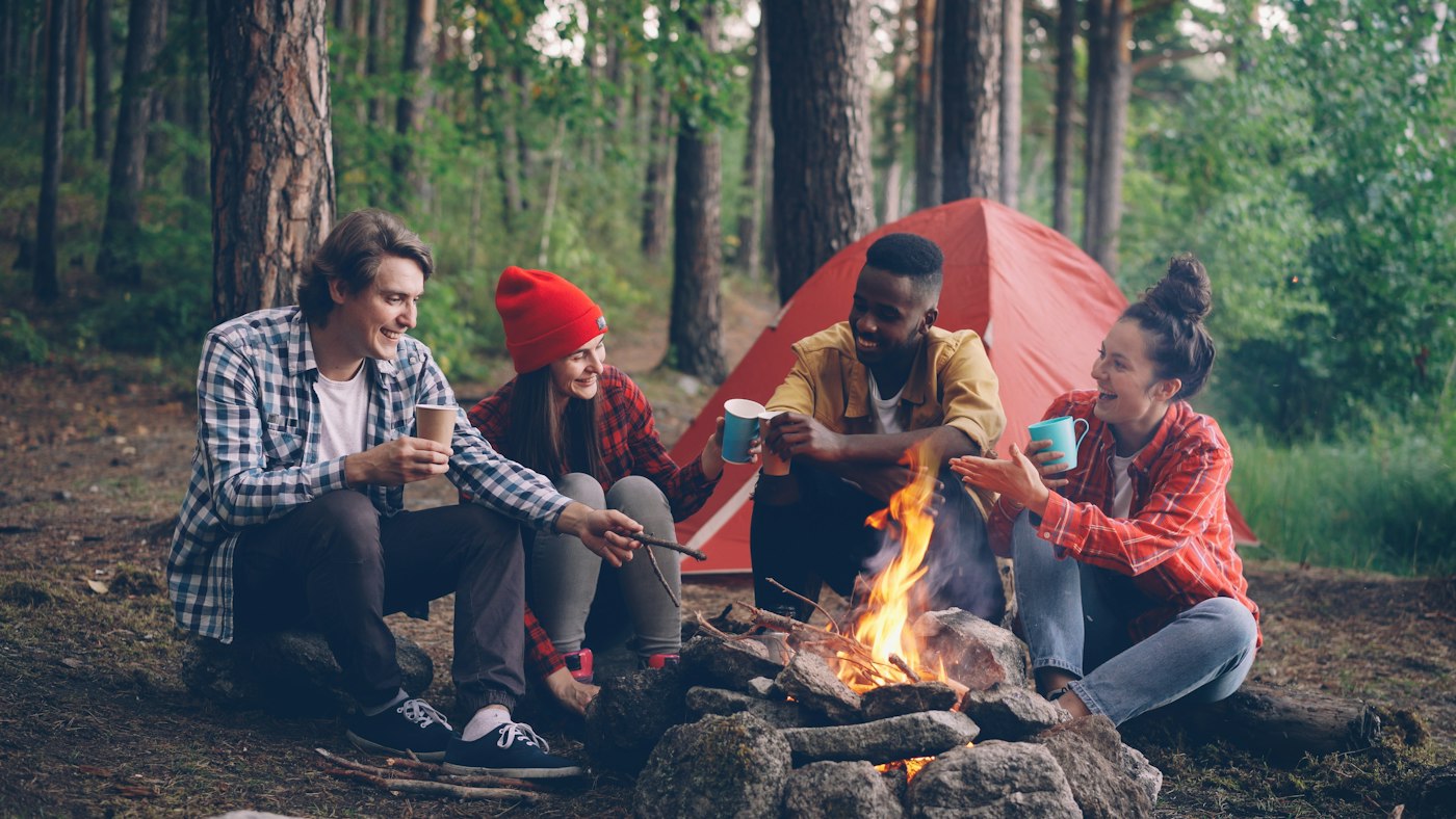 Real editorial photograph of friends gathering near forest campfire. Cover for Co-Creating a Gathering From Scratch
