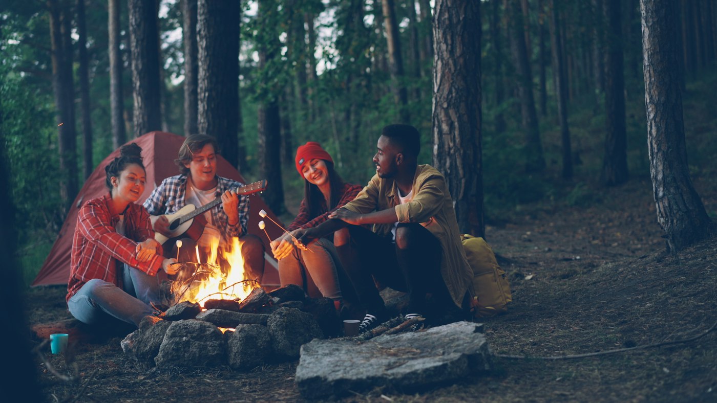 Real editorial photograph of friends playing guitar at forest campfire. Cover for The Talking Circle as a Tool for Listening