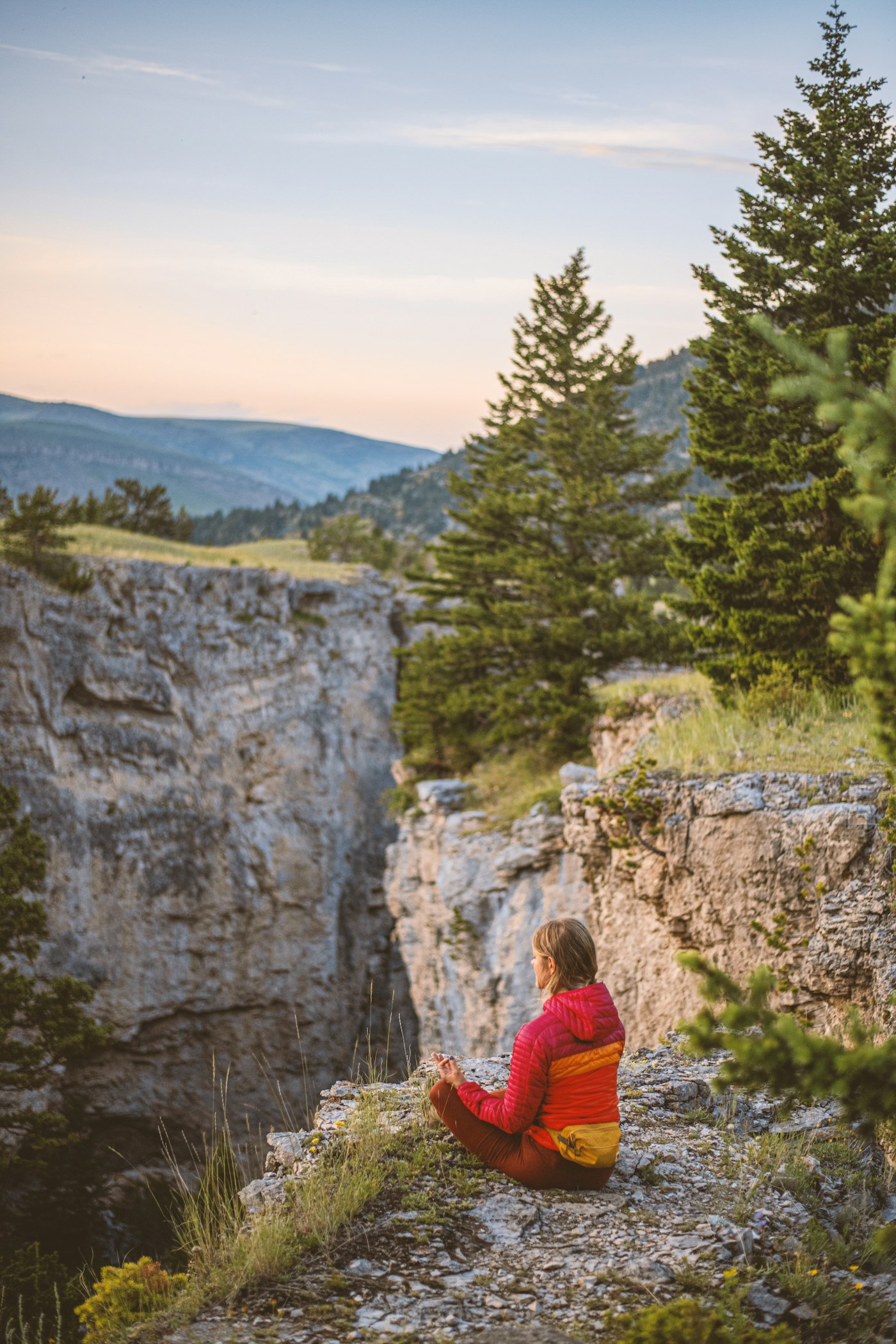 Real editorial photograph of person meditating on cliff next to forest. Cover for Sound Meditation: Listen Until the Room Feels Different
