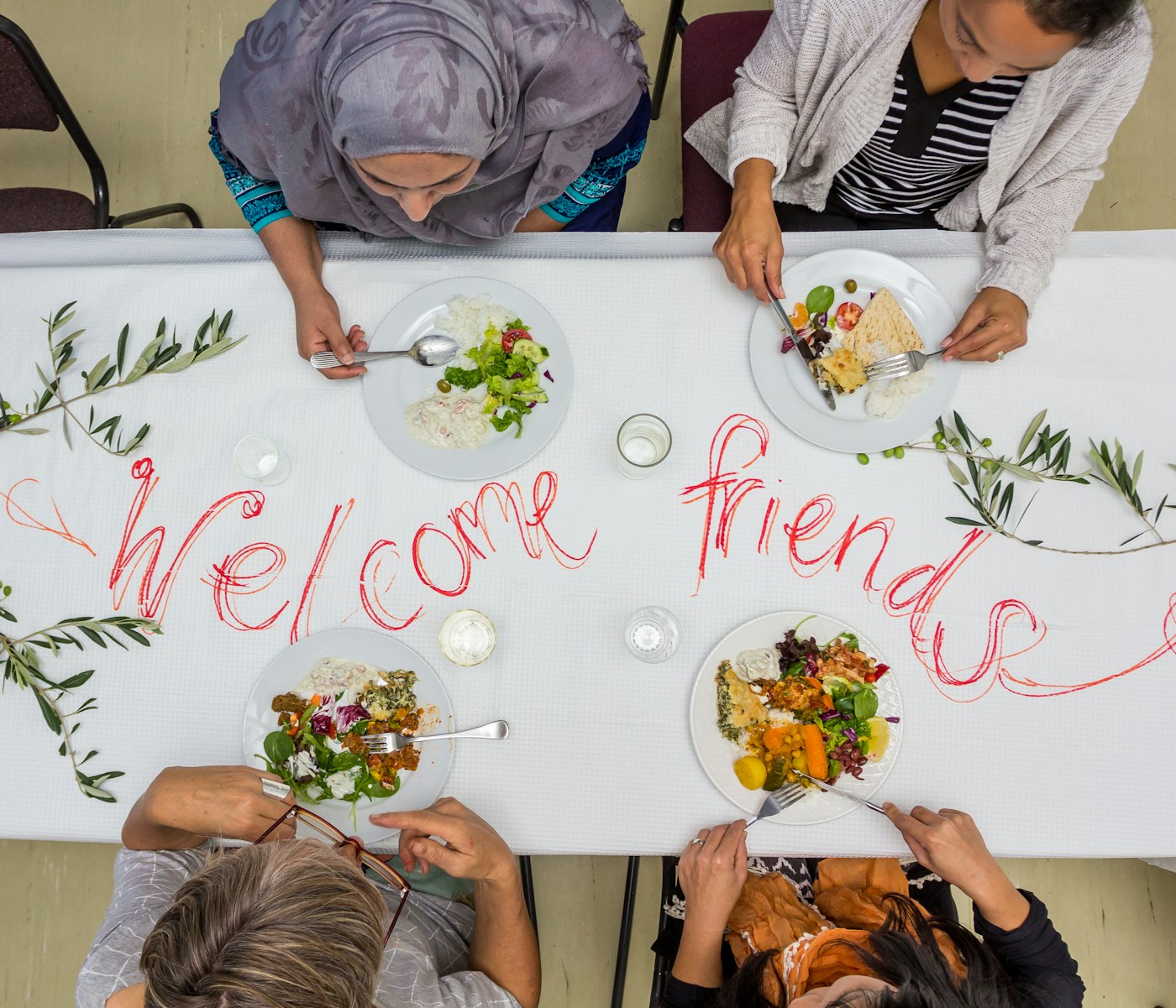 Real editorial photograph of community sharing food around a table. Cover for The First Ten Minutes of Belonging