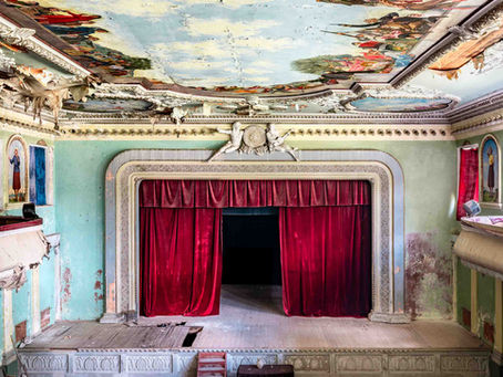 Ein prunkvolles, aber verfallenes Theater in Georgien mit rotem Samtvorhang, bunten Wandbemalungen und abblätternder Farbe.