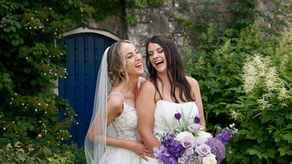 Lauren and Amy laughing together in the gardens of Farnham Castle on their wedding day