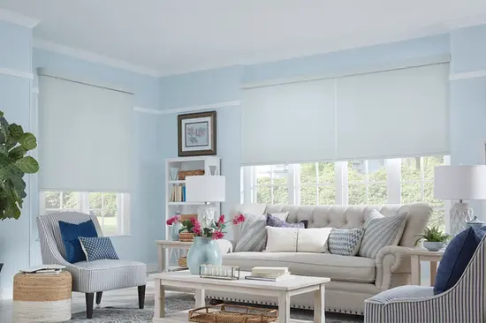 Bright living room with cordless Graber blackout roller shades in blue fabric, featuring a decorative contour valance.